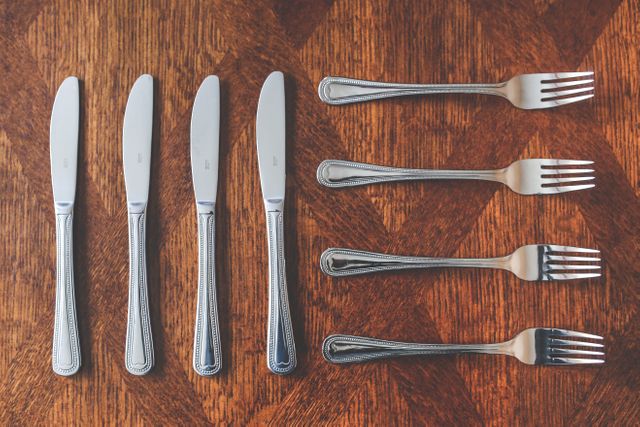 Silverware set including knives and forks, properly laid out on wooden surface, showing neat and organized arrangement. Suitable for illustrating dining settings, restaurant menus, kitchen organization blogs, interior decor, catering services, and hospitality industry promotions.