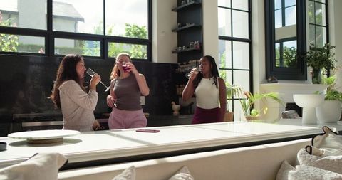 African american women and friends sipping wine, chatting at modern sunlit kitchen island