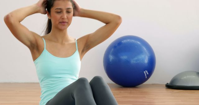 A woman doing sit-ups in a gym with an exercise ball in the background. She is exemplifying an active and healthy lifestyle, focusing on fitness and physical training. Ideal for use in fitness blogs, exercise tutorials, health magazines, workout guides, or promotional materials for gyms and wellness programs.