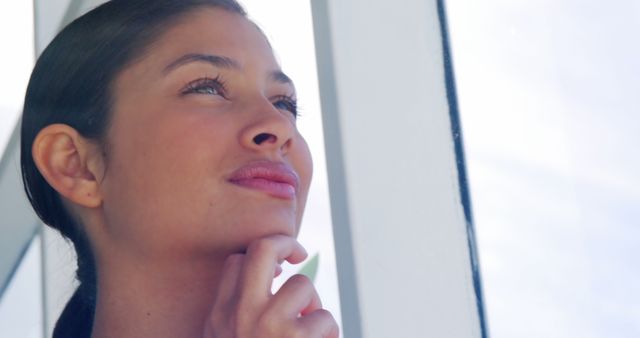 A young Hispanic woman appears contemplative as she gazes upwards, with copy space. Her expression suggests deep thought or daydreaming, adding a sense of introspection to the image.