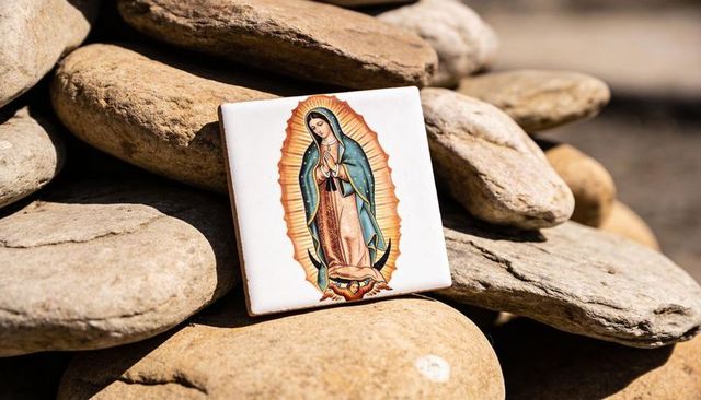 Sunlit virgin of guadalupe ceramic tile resting on river stones for folk shrine devotion
