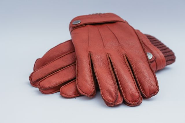Red leather gloves lying on a white background, showcasing detailed design and quality stitching. Ideal for use in articles about winter fashion, accessory trends, and cold weather essentials. Suitable for e-commerce sites, clothing stores, or fashion magazines to display stylish and trendy winter gloves.