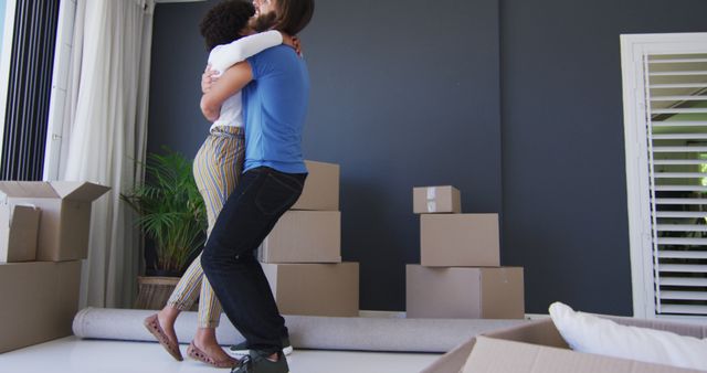 Couple embracing in their new home surrounded by moving boxes. Perfect image for themes of new beginnings, relationships, and moving day. Ideal for real estate articles, blogs focusing on moving tips, or advertisements for moving services.