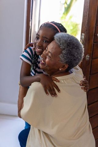 African american grandmother hugging granddaughter in doorway, joyful multigenerational bond