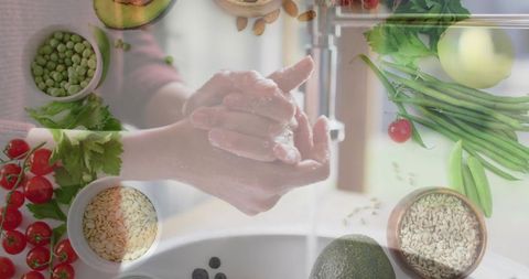 Washing hands with soap at kitchen sink surrounded by fresh produce and grains