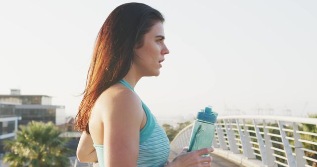 Caucasian woman drinking water from water bottle with copy space on white bridge in the morning. Excercising, jogging, sport and healthy lifestyle, unaltered.
