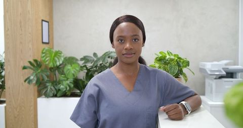 African american nurse standing at clinic reception wearing gray scrubs and smartwatch