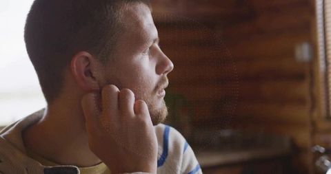 Man Adjusting Wireless Earbud in Cozy Wooden Cabin