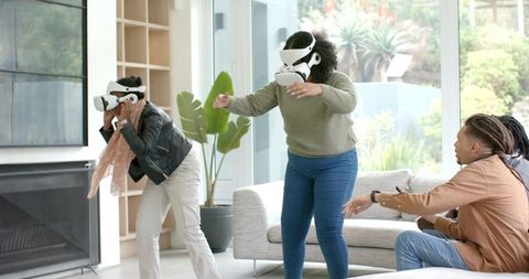 Multicultural friends playing virtual reality games in modern living room with VR headsets