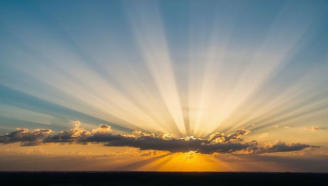 Radiating Sunrise Casting Crepuscular Rays Across Cloud-Held Horizon