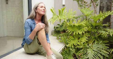 Senior Woman Relaxing Outdoors with Modern Home and Greenery