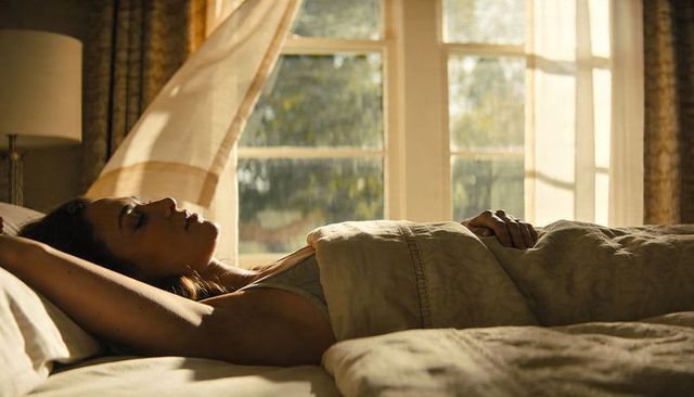 Woman resting in bed during rain-streaked morning light, serene bedroom moment