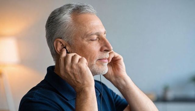 Senior man enjoying music with wired earphones, eyes closed, cozy living room warm glow