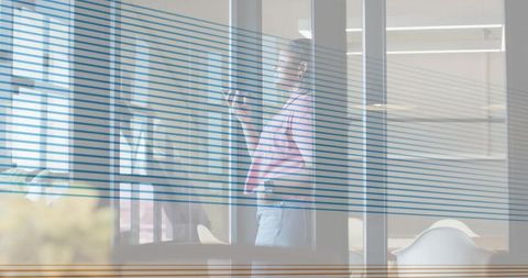 Businesswoman standing behind glass partition holding smartphone, wearing pink top, jeans