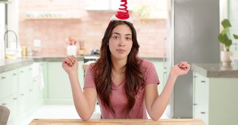 Cheerful woman shrugging at kitchen table with red spiral headband