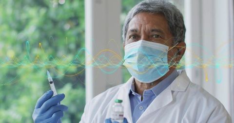 Senior physician preparing vaccine syringe beside clinic window wearing mask and gloves