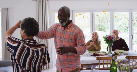 Dancing friends celebrating casual home dinner party with confetti, flowers, sunlight