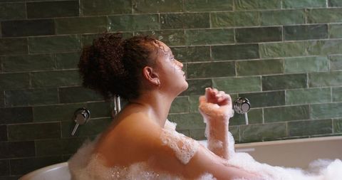 African american woman relaxing in bubble bath with green subway tiles and chrome faucets