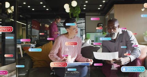 Coworkers reviewing documents with floating ui tags and laptop in modern office lounge