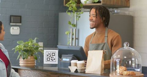 Smiling barista serving takeout coffee at modern cafe counter with qr code