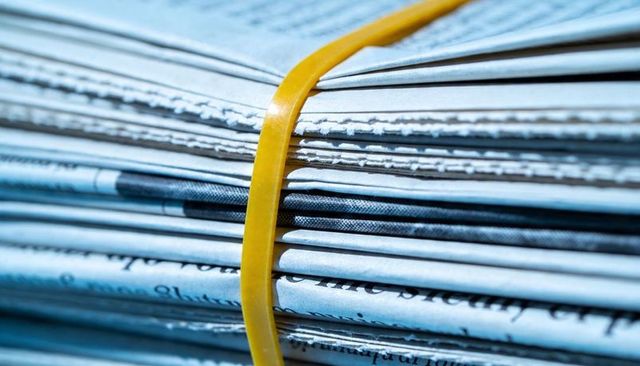 Stacked newspapers bound by yellow rubber band — macro closeup showing halftone print and paper fibe