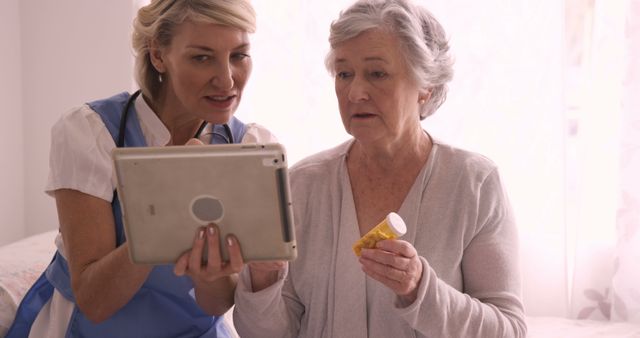 Caregiver and senior woman interacting in a home setting. The caregiver uses a digital tablet to explain how to administer medication. Perfect for illustrating healthcare services, elderly care, home nursing, or medical assistance.