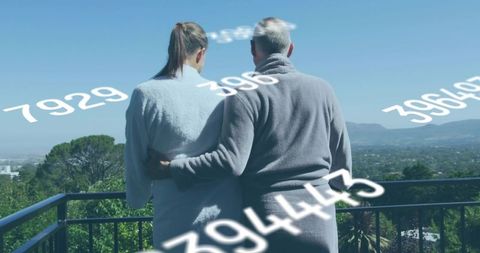 Senior couple embracing on balcony with floating numeric overlay overlooking sunlit valley
