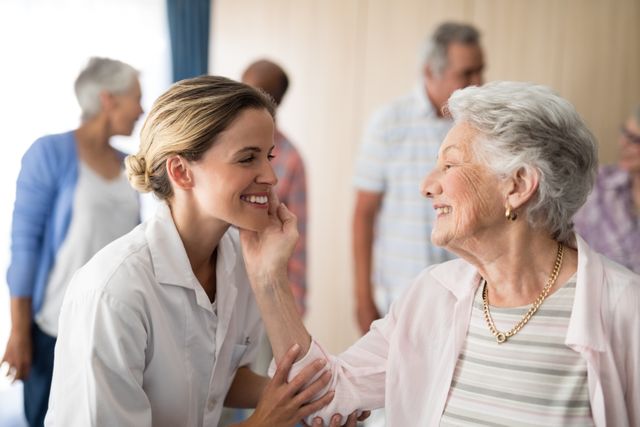 Senior woman touching smiling female doctor in a retirement home, showcasing a positive and supportive environment. Ideal for use in healthcare, elderly care, and senior living promotional materials, as well as articles and advertisements focusing on patient care and medical professionals.