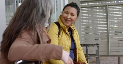 Middle-aged women laughing and chatting on bench at urban transit shelter