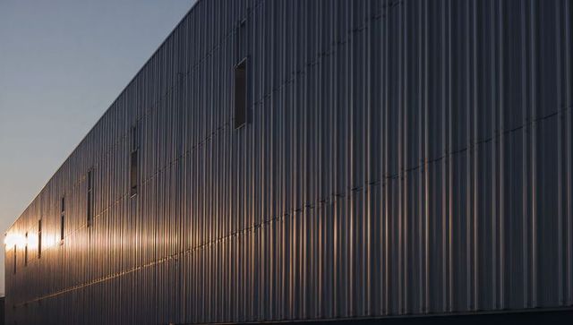 Corrugated metal facade reflecting golden sunset on industrial warehouse wall