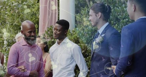 Men chatting at garden ceremony wearing suits and boutonniere with network overlay