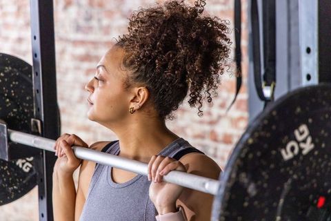 African american woman lifting barbell on shoulders in urban gym, focusing on strength training