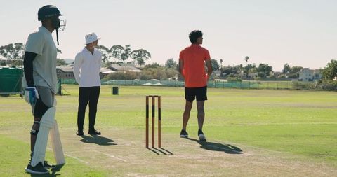 Indian cricketer bowling on sunny field practicing fast bowling technique with teammates