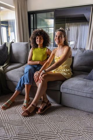 Sitting together, diverse friends relaxing on gray sofa wearing sandals and summer outfits