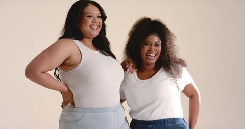 Smiling plus-size friends wearing white tops and jeans celebrating confidence, friendship