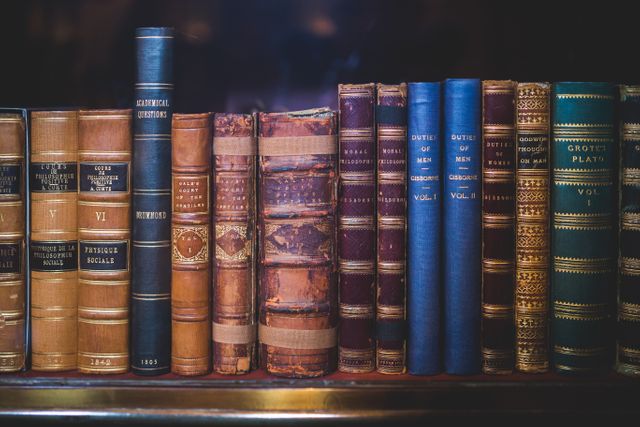 A visually captivating display of vintage leather-bound books arranged on a wooden shelf. Ideal for projects relating to education, literature, history, and nostalgia. Suitable for use in websites, blogs, or publications focused on classic literature and antique collections.