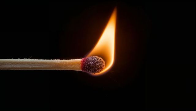 Single burning match close-up with bright flame and glowing ember on black background