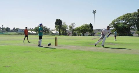 Cricket players sprinting between wickets on sunny suburban green field