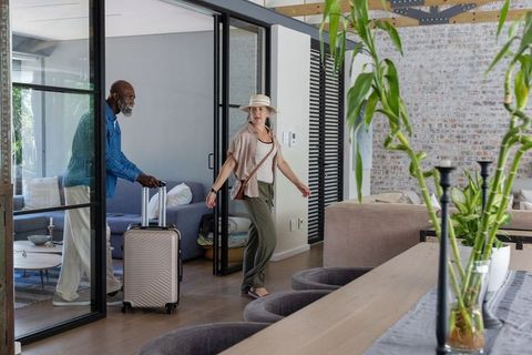 Mature couple arriving at modern loft, woman looking back while man pushing suitcase