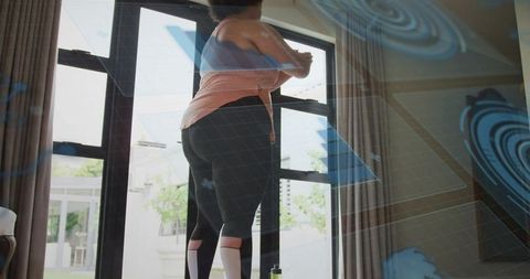 Curvy woman stretching by patio glass doors wearing peach top and black leggings, home workout