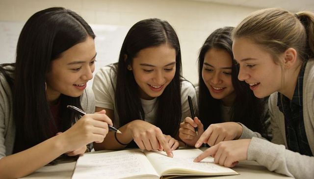 Female Students Collaborating and Studying Over Notebook in Classroom