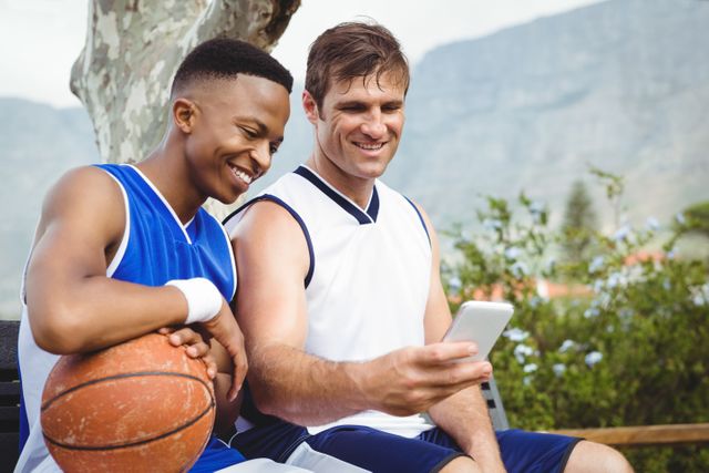 Smiling friends taking selfie while sitting in basketball court
