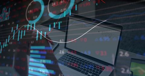 Laptop workstation displaying overlaid candlestick charts and market tickers for trading