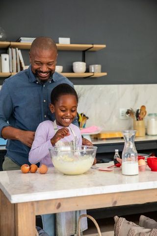 African american father guiding daughter whisking batter on kitchen island baking moment