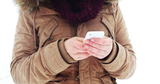 This image is ideal for illustrating themes related to technology, winter activities, and outdoor communication. It conveys a sense of staying connected and engaged with mobile devices even in cold weather. It could be used in a blog post about winter smartphone usage tips, a tech advertisement, or social media campaigns focusing on staying connected.
