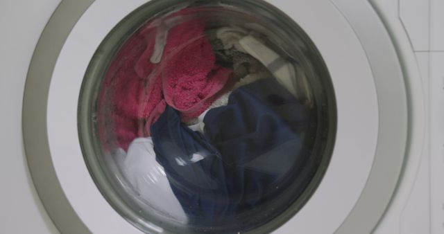 Close-up of clothes spinning inside washing machine. Useful for articles, ads, and content about household chores, cleaning appliances, energy-efficient laundry routines, or detergent brands.