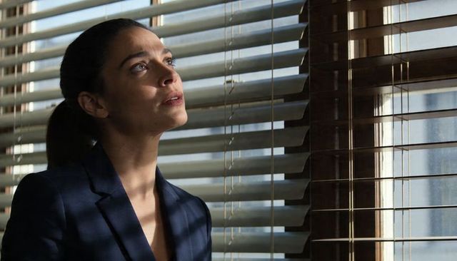 Gazing businesswoman at office window with venetian blinds casting light stripes