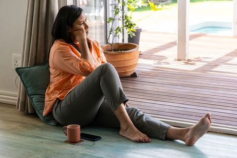 Mature woman sitting by sliding door gazing at pool in contemplative home lifestyle moment