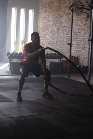 African american athlete performing battle rope workout in industrial gym building power