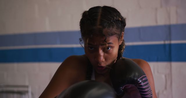 Female boxer concentrating during intense training session in the gym. Ideal for fitness, sports, boxing event promotions, motivational content, martial arts classes, and health campaign materials.
